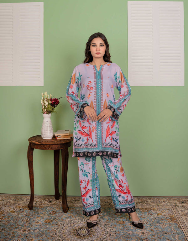 Woman wearing a floral outfit standing in front of a green wall with a small table and vase.