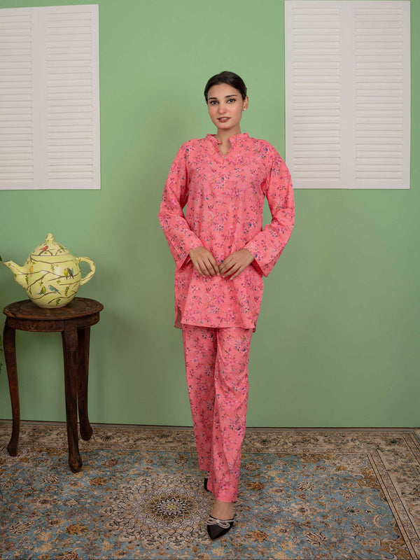 Woman in a pink traditional outfit standing in a room with a green wall and a small table with a teapot.